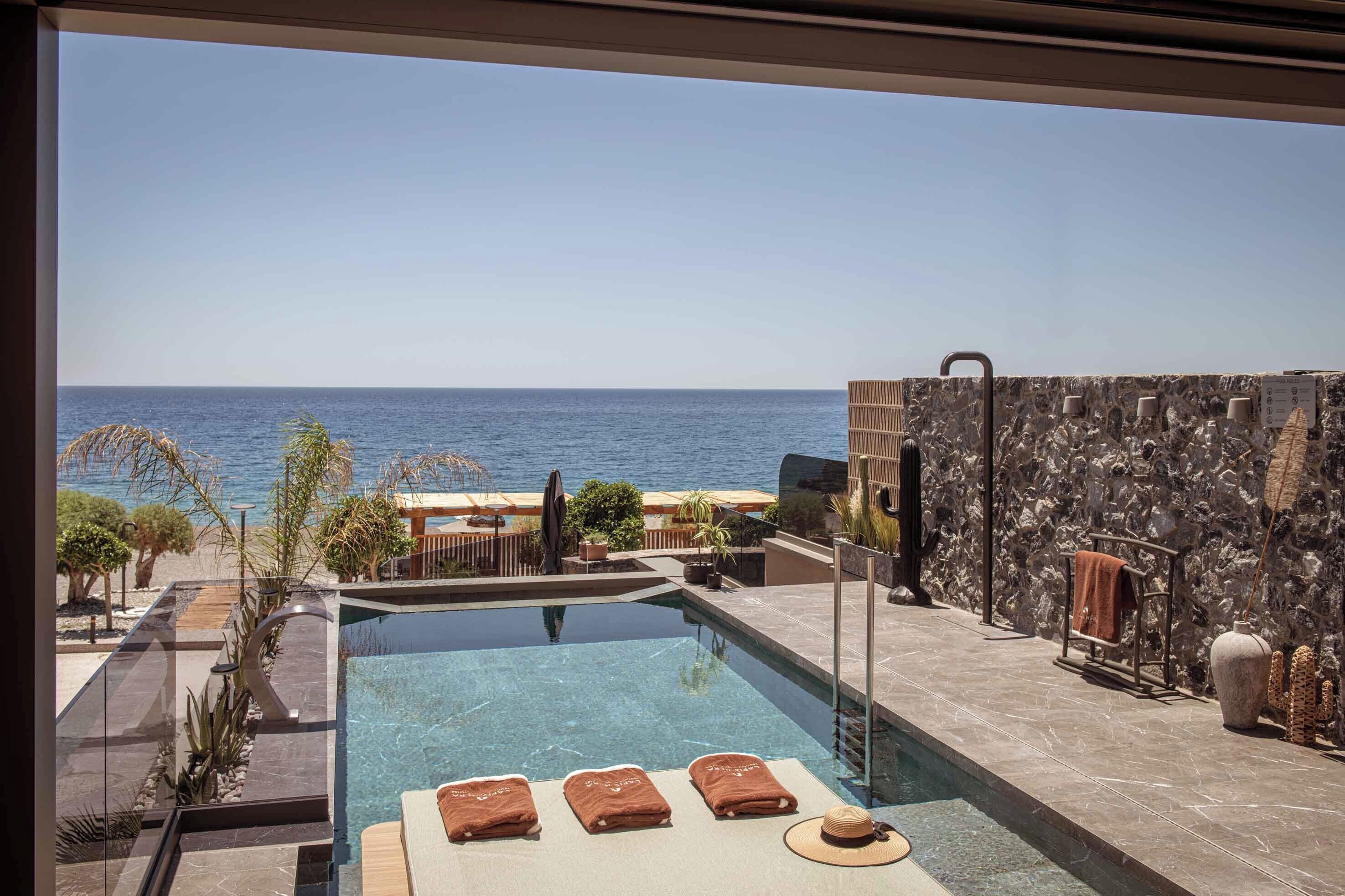 A pool area with clear blue water, a stone wall, and a view of the sea.