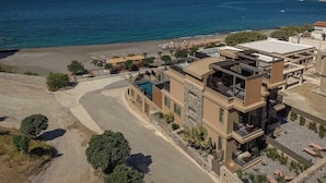 Um edifício moderno de vários andares com piscina no terraço, situado perto de uma praia com águas azul-claras.