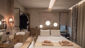 Quarto de hotel moderno com uma cama grande, mesas de cabeceira, penteadeira com espelho e banheiro.
