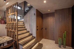 A modern staircase with wooden railings and integrated lighting, leading to a landing with a wooden door and a potted cactus plant. - Lapis Nera Villas - Beachfront & Free*Heated Pools (Heraklion)