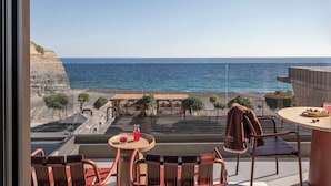 Varanda com vista para o mar, uma mesa com bebida e uma cadeira.
