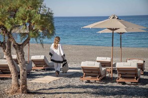 Ein Strandabschnitt mit Liegestühlen, einem großen Sonnenschirm und einer Person, die gerade geht.