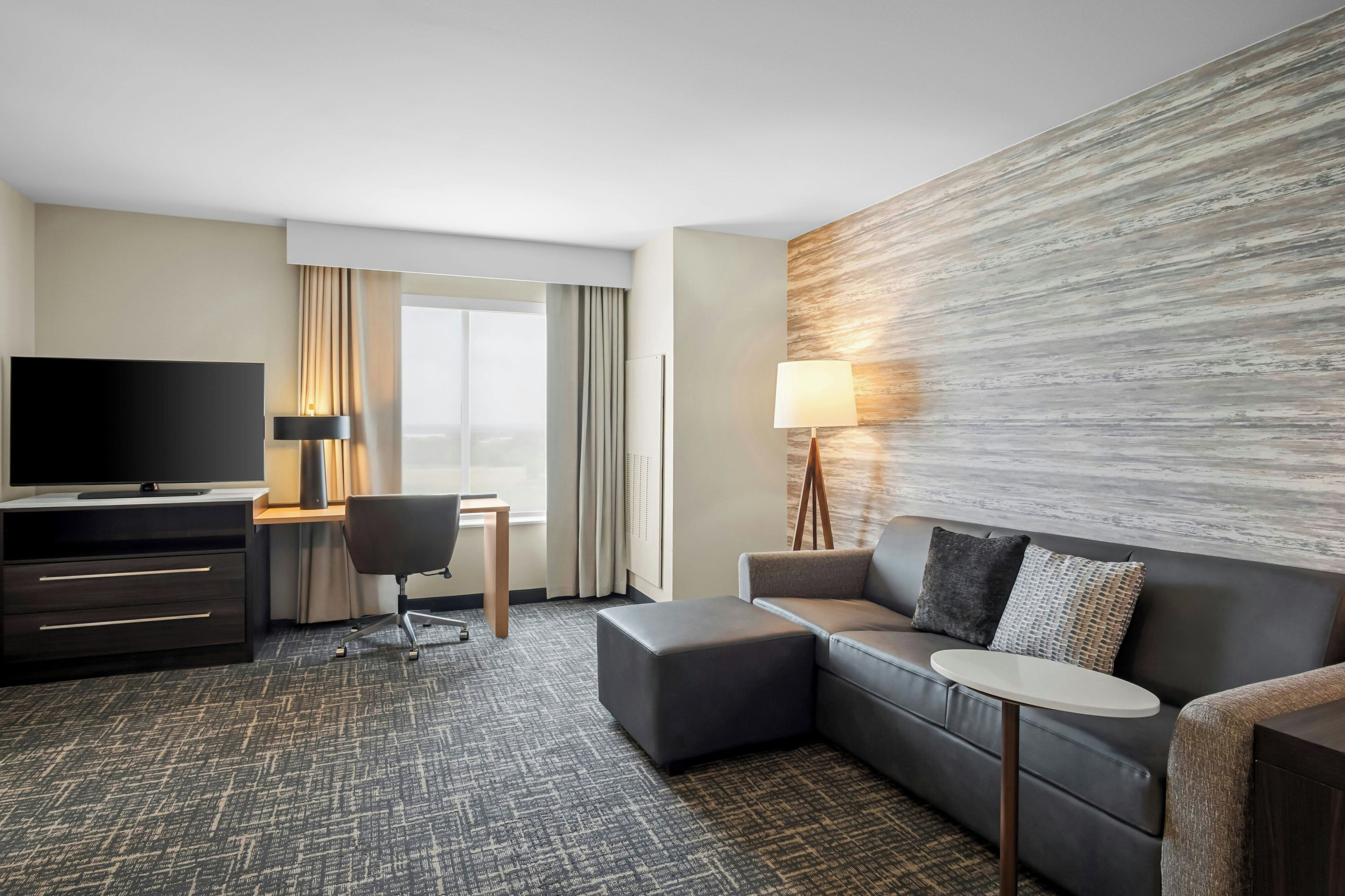 A hotel room with a sofa, a TV, a desk, and a lamp.