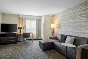 Habitación de hotel con sofá, televisión, escritorio y lámpara.