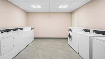 A laundry room with white appliances, including washers and dryers, and a tiled ceiling.