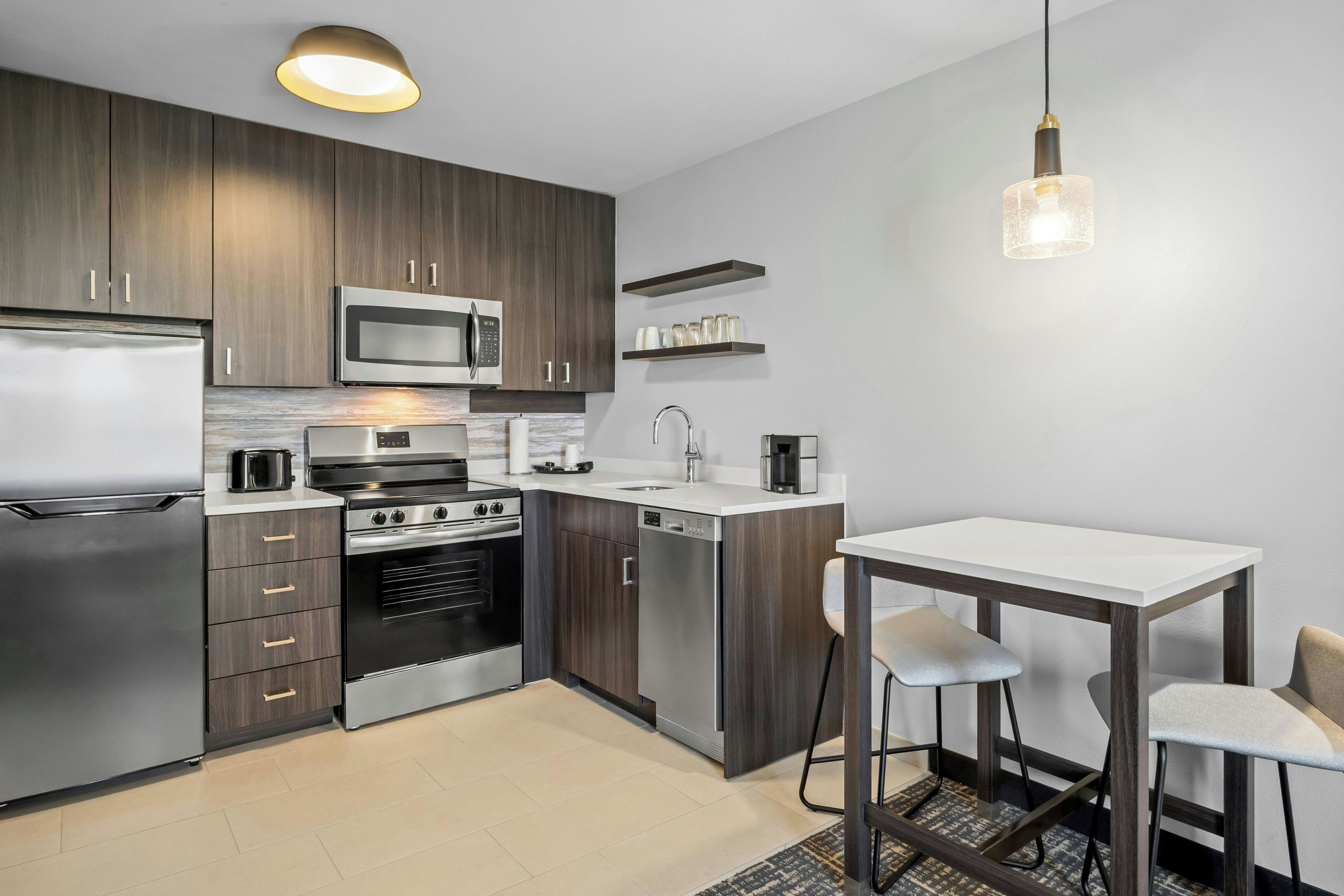 A modern kitchen with stainless steel appliances, a microwave, a built-in oven, and a dishwasher. There is a bar counter with stools and a hanging light fixture.