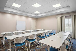 A conference room with white tables, blue chairs, a whiteboard, and a door.
