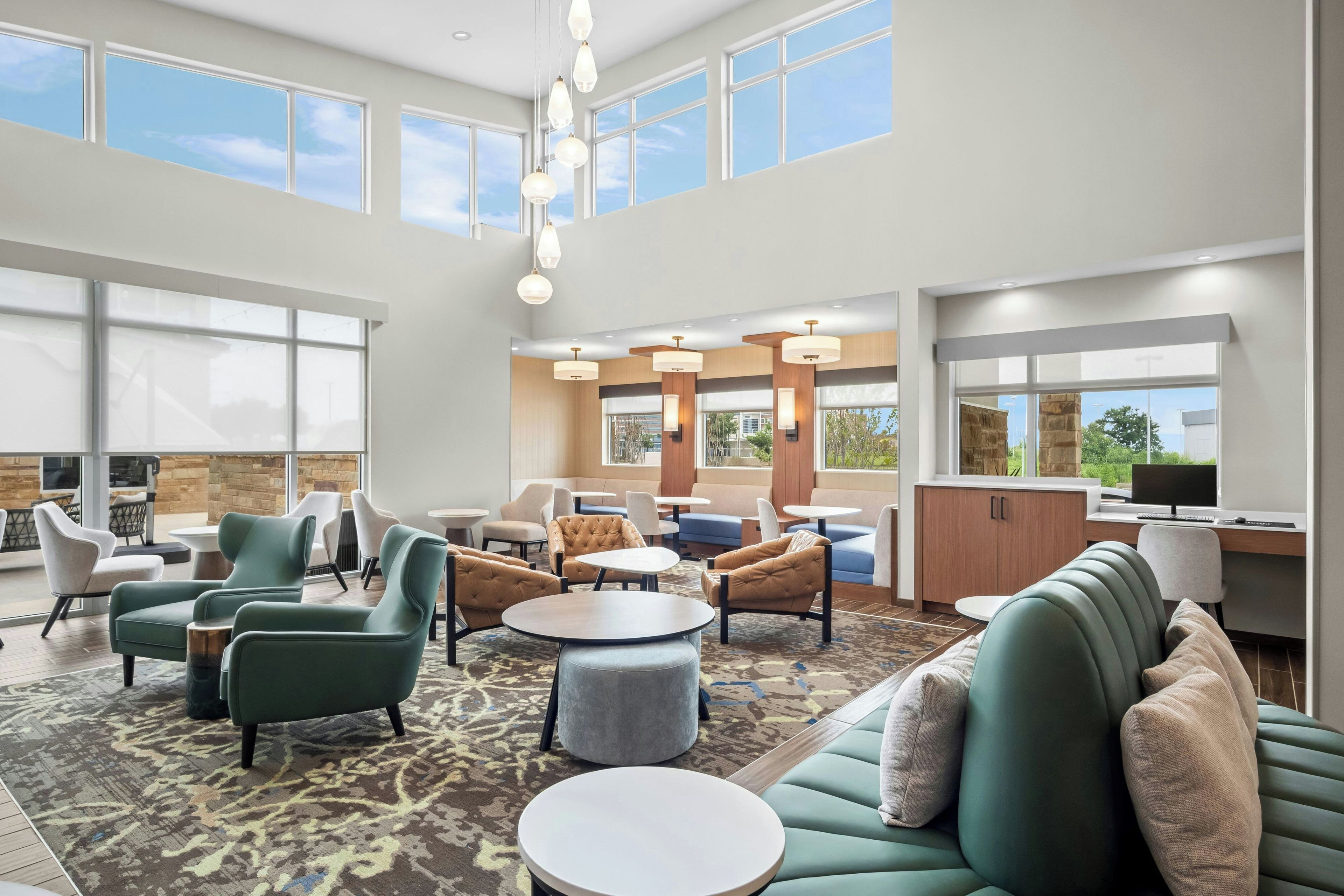 En rummelig hotellobby med højt til loftet, store vinduer og forskellige siddepladser, herunder sofaer og stole.