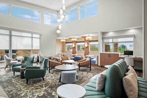Un amplio vestíbulo de hotel con techos altos, ventanas grandes y diversas opciones de asiento, incluyendo sofás y sillones.