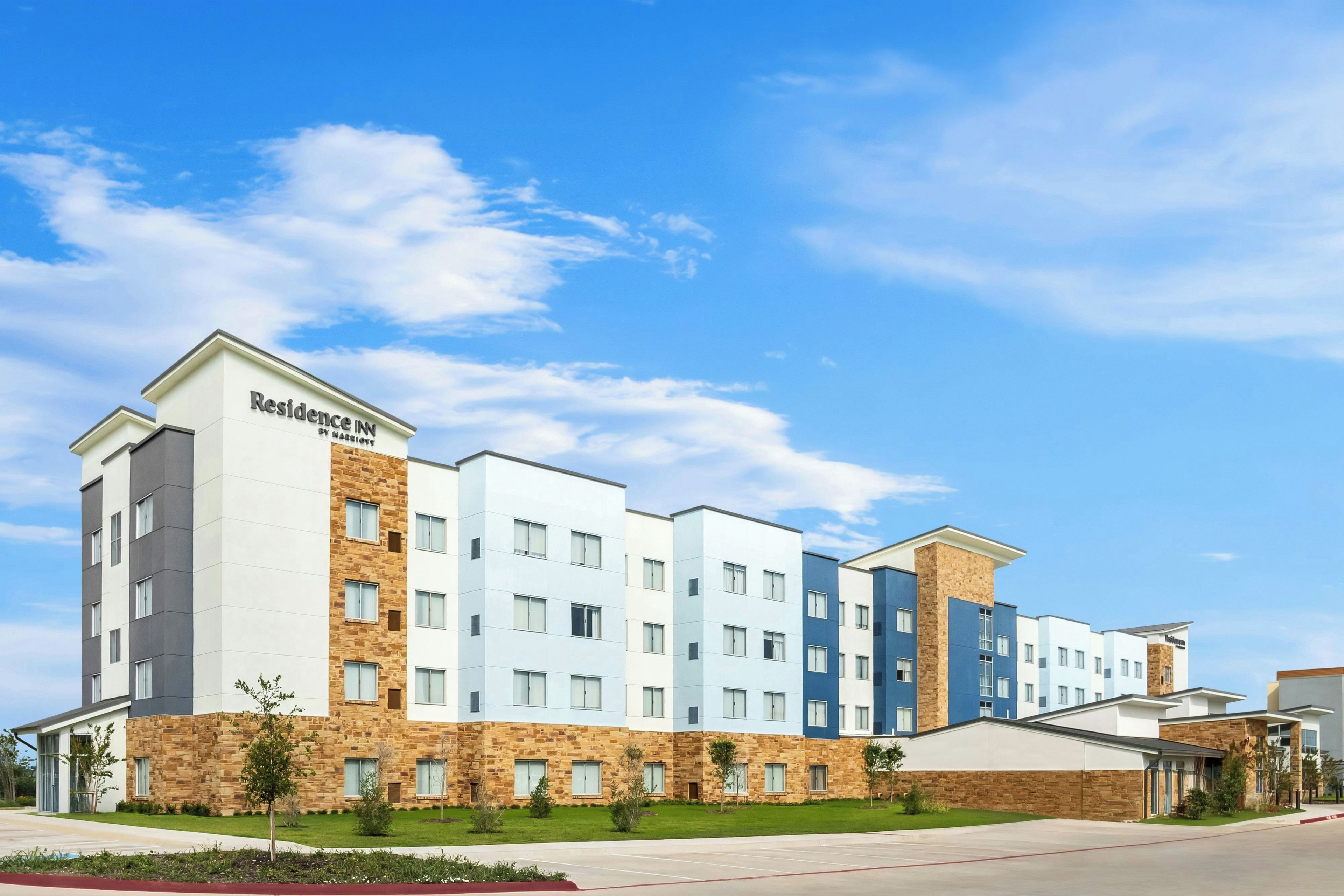 Un edificio de hotel de varios pisos con techo plano y una combinación de fachadas de piedra y pintadas.