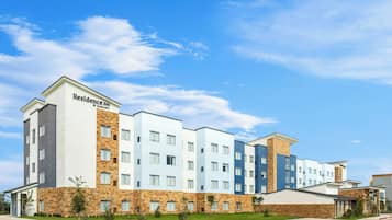 Un edificio de hotel de varios pisos con techo plano y una combinación de fachadas de piedra y pintadas.