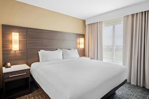 Una habitación de hotel con una cama grande, mesitas de noche, una lámpara y una ventana con cortinas.