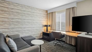Habitación de hotel con sofá, escritorio, silla, televisión y ventana con cortinas.