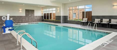 An indoor swimming pool with clear water, a lifeguard chair, and a pool ladder.