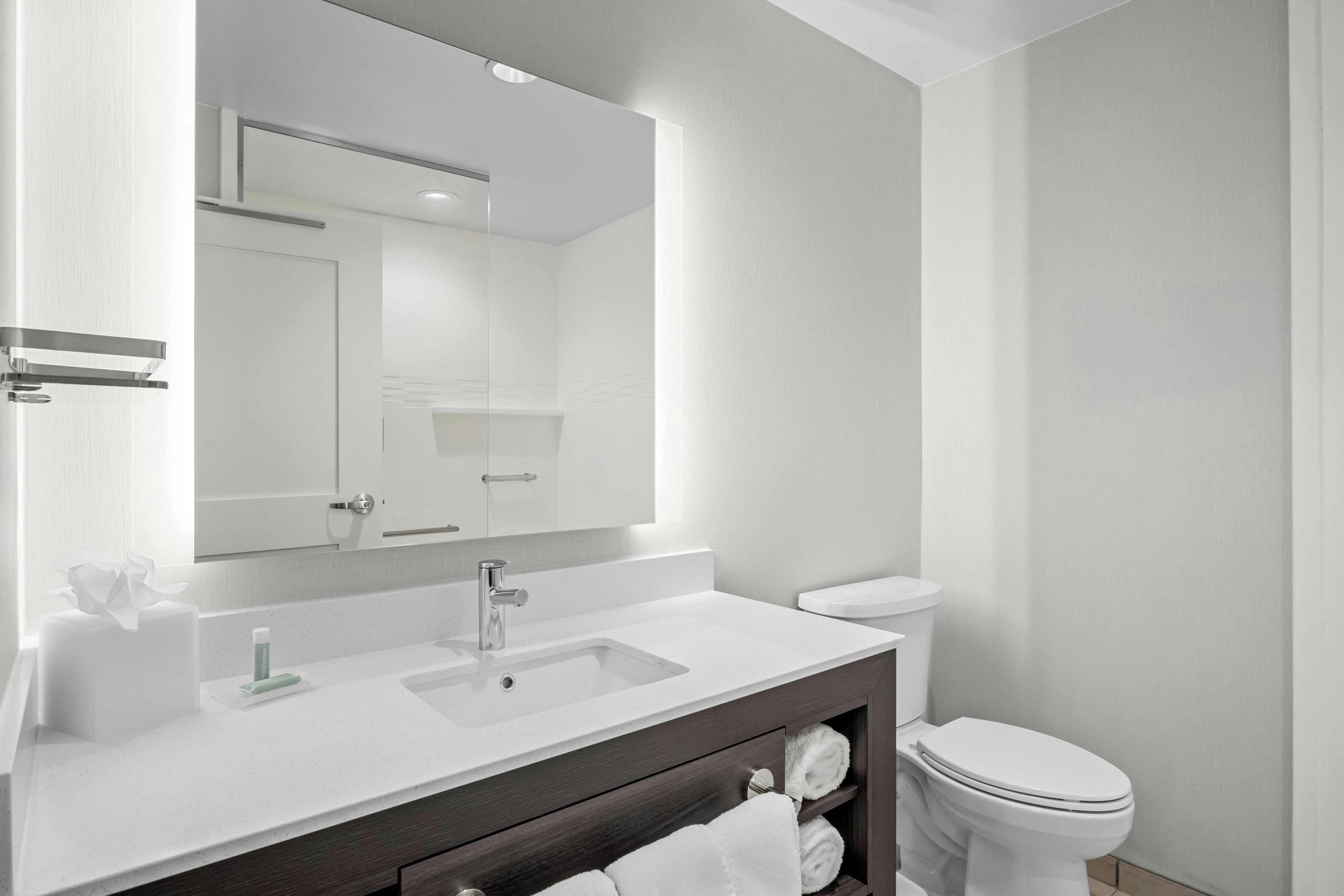 A modern bathroom with a white sink, a mirror, a toilet, and a towel rack.