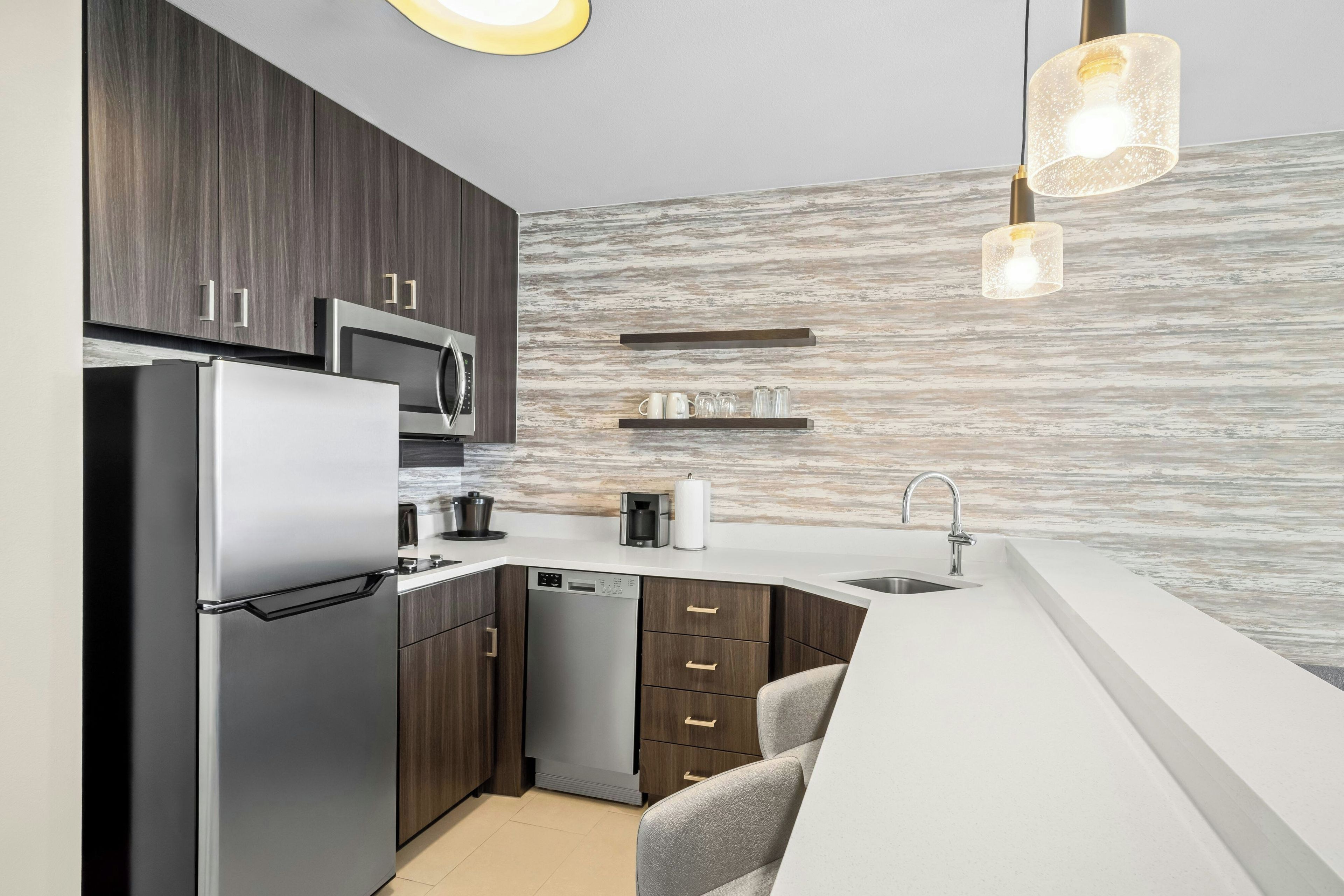 A modern kitchen with dark wood cabinets, stainless steel appliances, a dishwasher, and a white countertop.