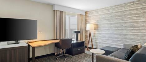 Une chambre d’hôtel équipée d’un téléviseur à écran plat, d’un bureau, d’une chaise, d’un canapé, d’une petite table ronde et d’une lampe.