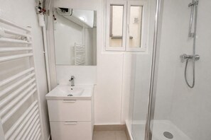 Ein Badezimmer mit weißem Waschbecken, einem Spiegel, einer Dusche inklusive Handbrause und einem Handtuchhalter.