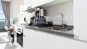 A modern kitchen with white cabinetry, a stainless steel sink, and a coffee maker. - Bloomfields CharmingStu Samana view (Dubai)