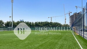 A sports field with a goalpost, surrounded by a fence and construction cranes in the background. - Bloomfields CharmingStu Samana view (Dubai)