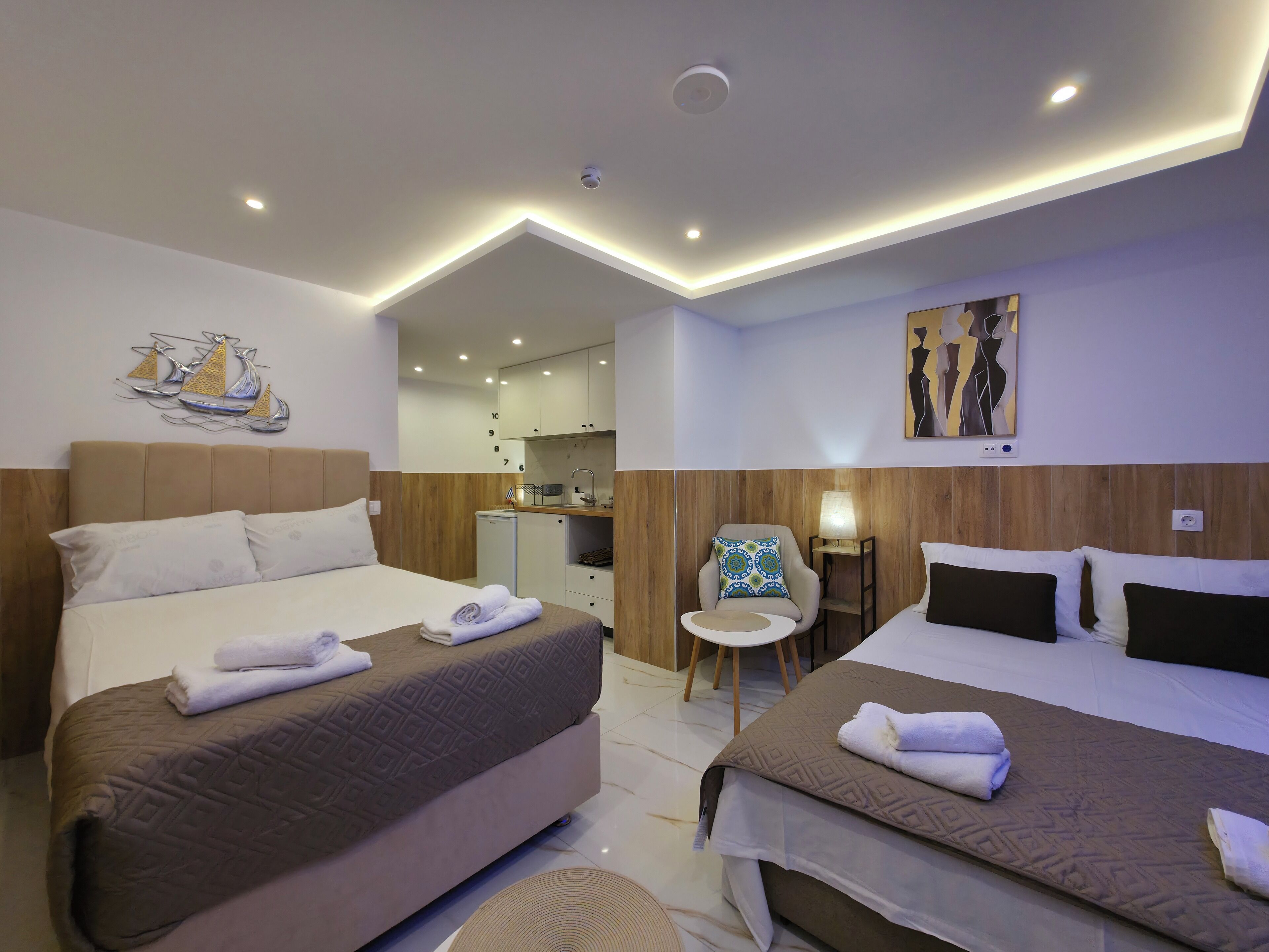 A hotel room with two beds, a small kitchenette, a seating area, and artwork on the walls.