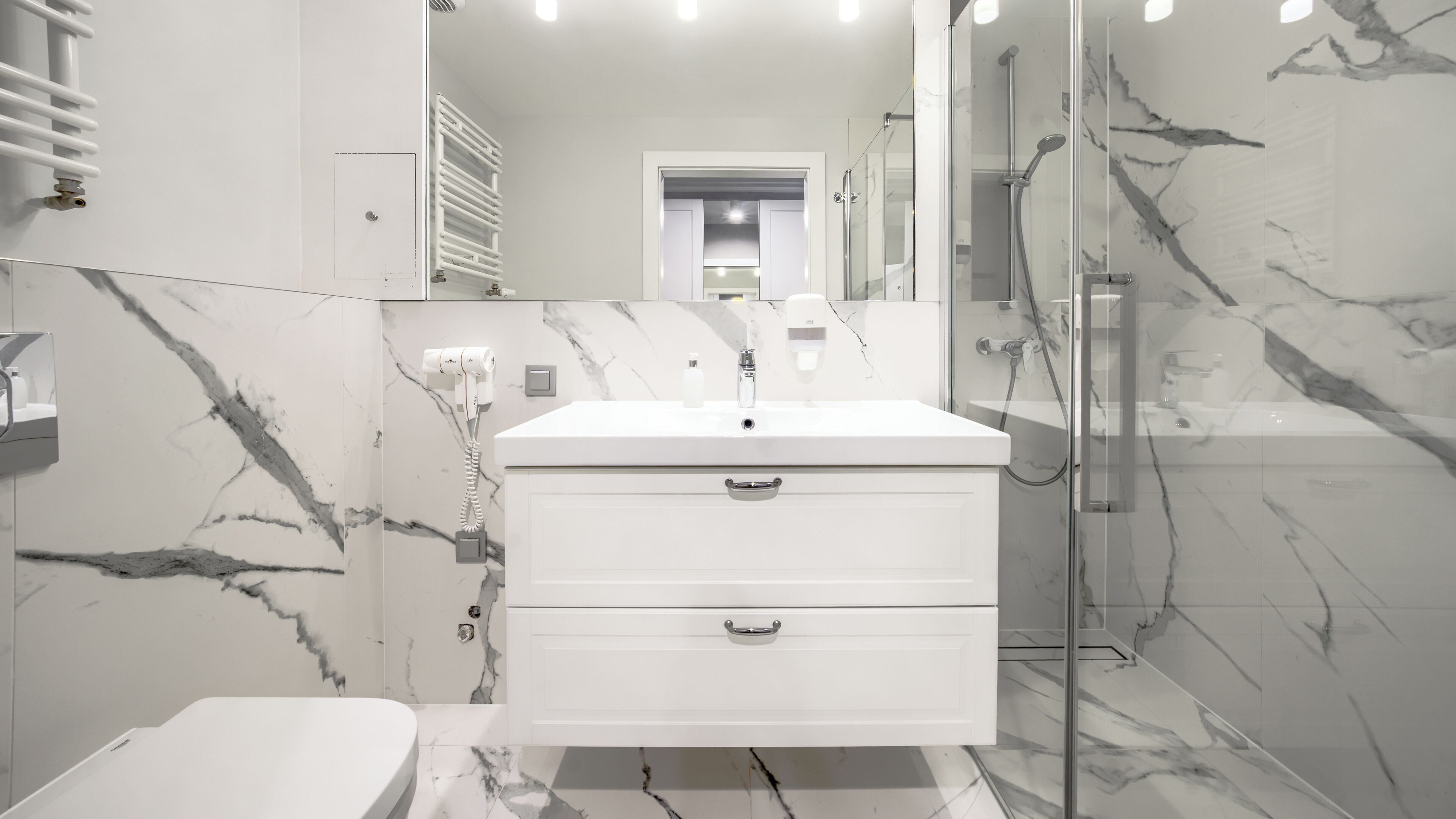 Un bagno moderno con un mobile lavabo bianco, cabina doccia in vetro e pareti in marmo.