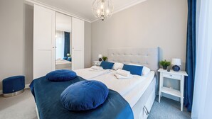 A modern bedroom with a large bed, two bedside tables, a mirror, and a chandelier. - Apartamenty Sun & Snow Rubus (Świnoujście)