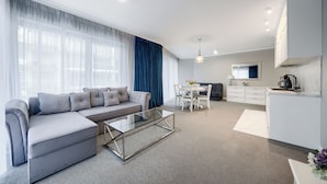 A modern living room with a grey sofa, a glass coffee table, and a dining area with a white table and chairs. - Apartamenty Sun & Snow Rubus (Świnoujście)