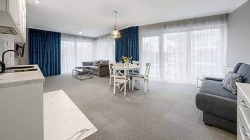 A modern living room with a grey sofa, a dining table with chairs, and a kitchen area with a white countertop.