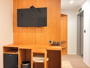 Ein Holztisch mit einem darüber angebrachten Fernseher, ein kleiner Kühlschrank und ein Mülleimer.