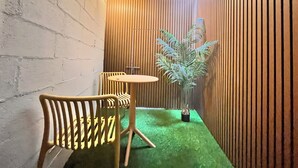A small, enclosed space with a green carpet, wooden slatted walls, a potted plant, and a table with chairs. - OnKorea Stay (Seoul)