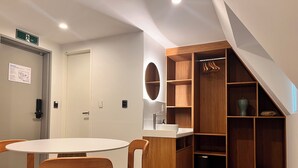 A modern room with a round table, two wooden chairs, a wooden wardrobe with hanging space, a mirror, and a sink. - OnKorea Stay (Seoul)
