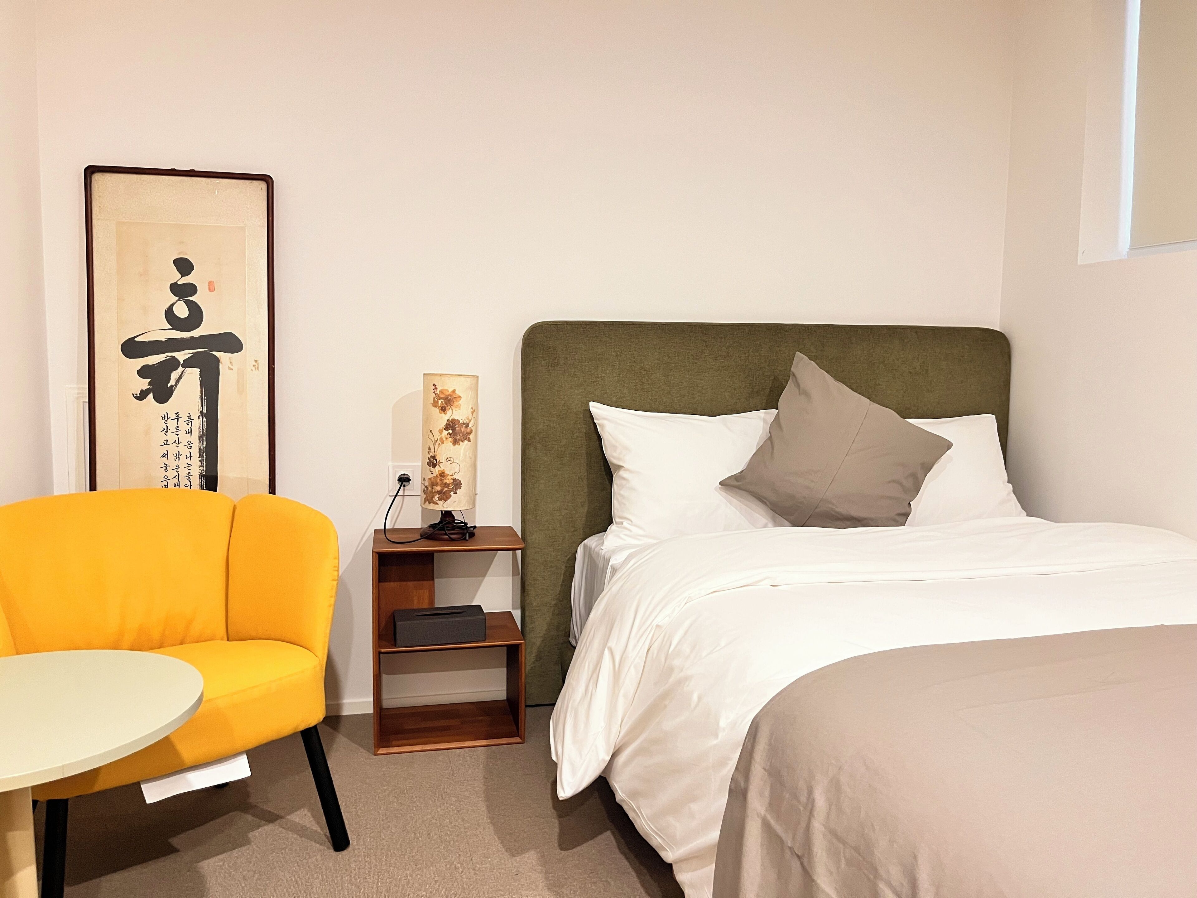 Une chambre d’hôtel avec un lit, une table de chevet avec une lampe, une chaise et une œuvre d’art encadrée au mur.