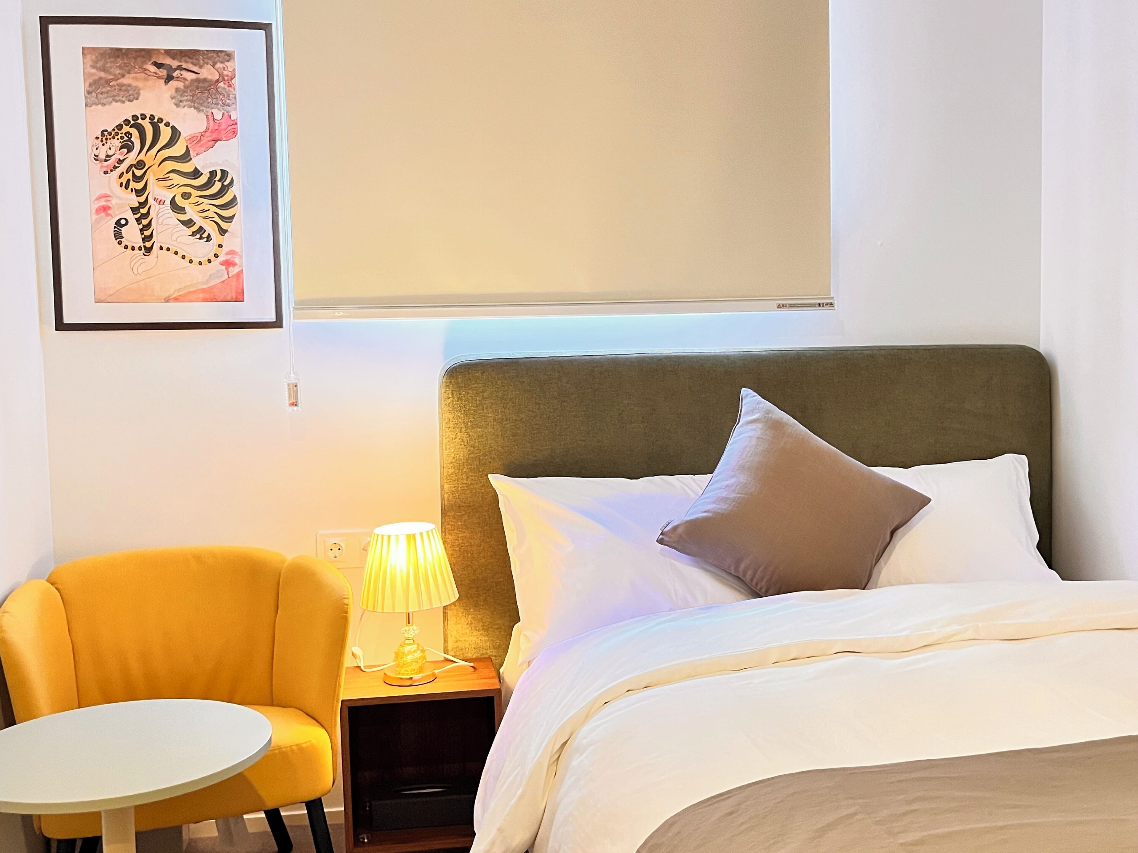 A hotel room with a bed, a nightstand with a lamp, a chair, and a framed picture on the wall.