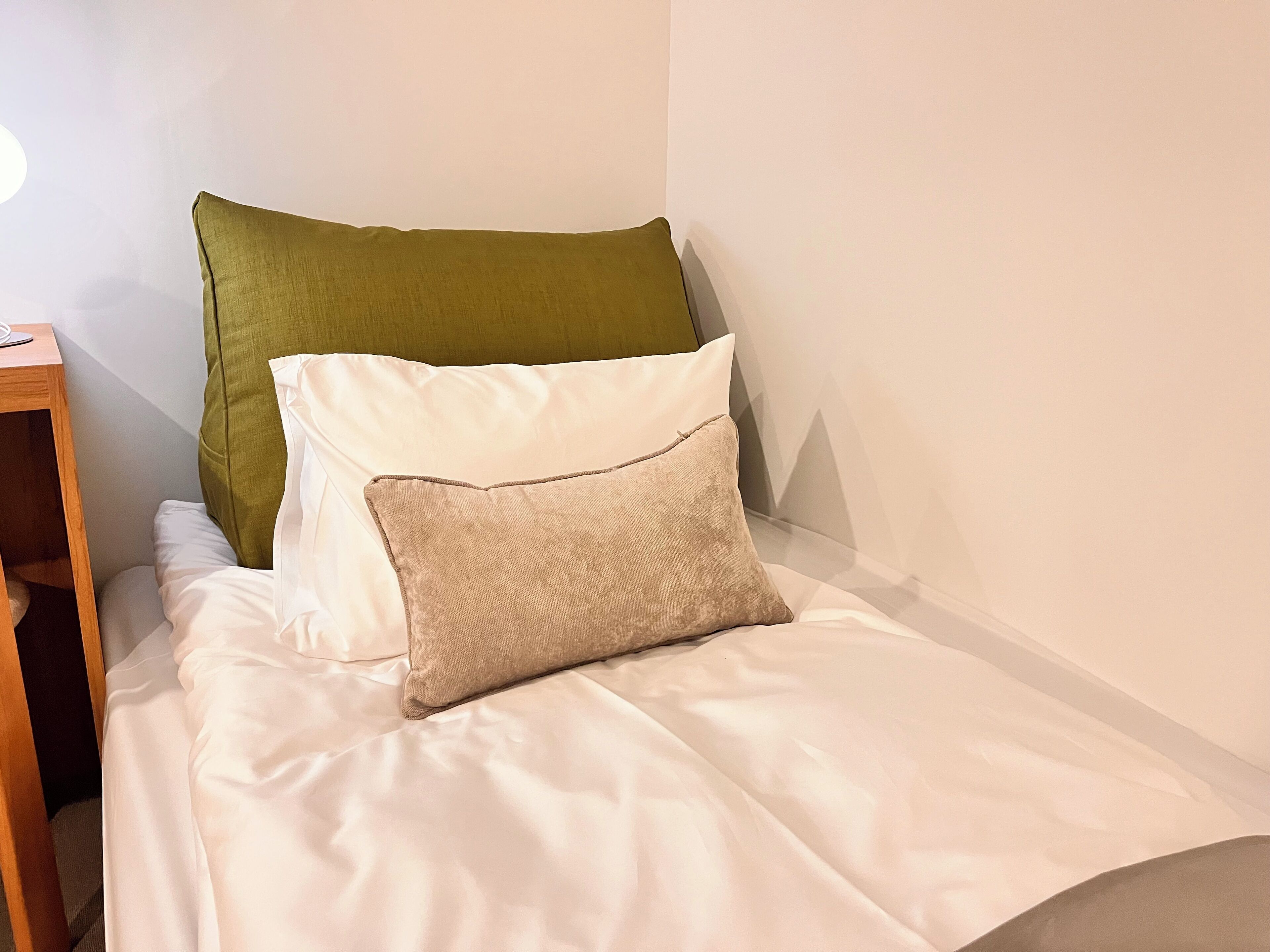 A bed with white bedding and two pillows, one green and one beige.