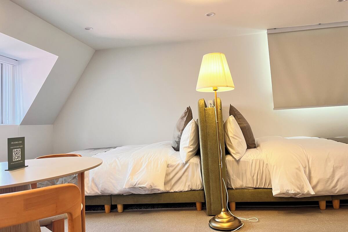 A hotel room with a bed, a standing floor lamp, a small round table, and a window.