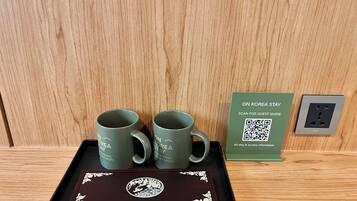 Uma bandeja com duas canecas verdes, uma placa com código QR e uma tomada em uma superfície de madeira.