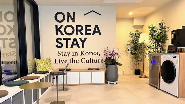 A modern interior with a sign reading 'ON KOREA STAY,' a laptop on a desk, a washing machine, and potted plants. - OnKorea Stay (Seoul)