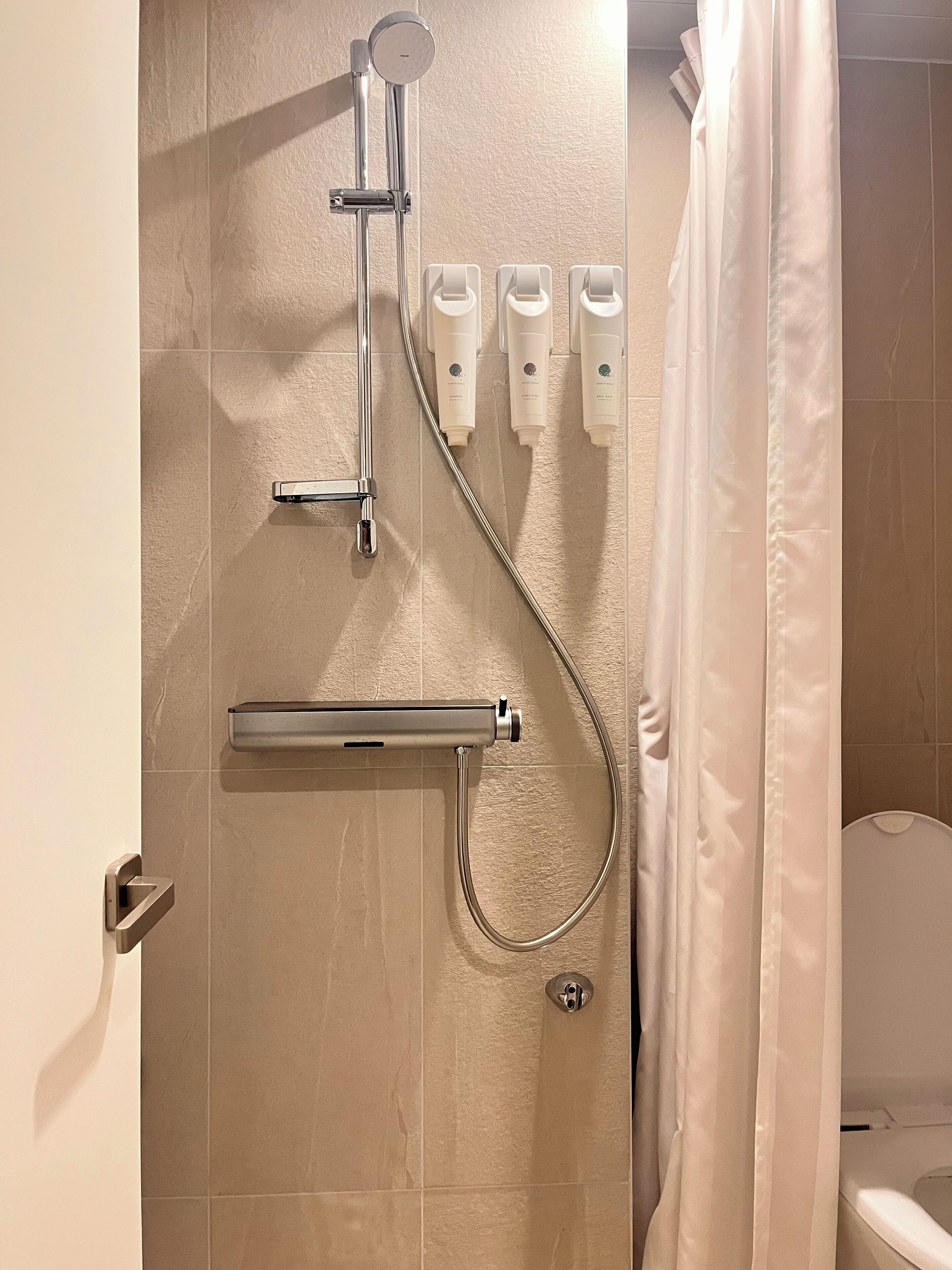 Ducha con cabezal de ducha manual, accesorio de ducha manual y tres botellas de champú o acondicionador en la pared.