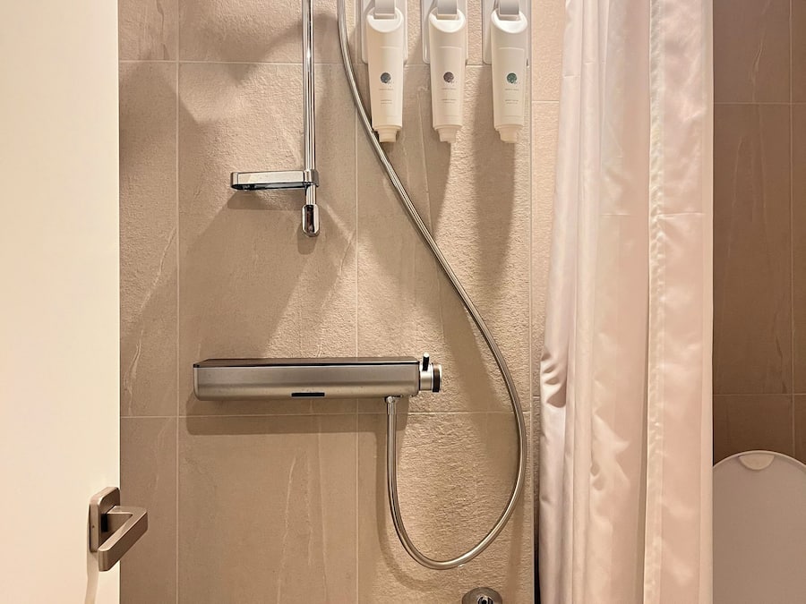 Ducha con cabezal de ducha manual, accesorio de ducha manual y tres botellas de champú o acondicionador en la pared.