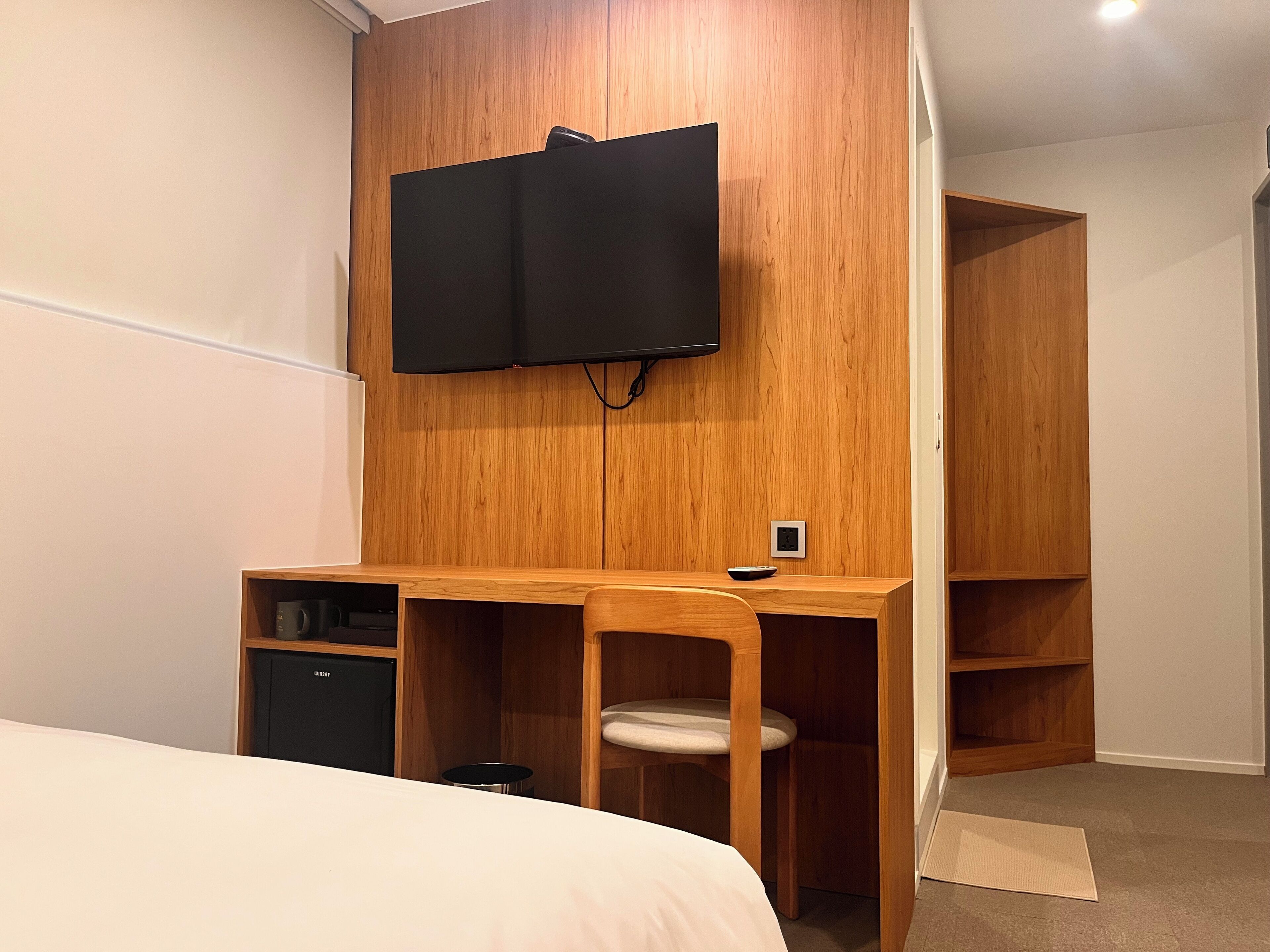 A bedroom with a wooden desk, a television mounted on the wall, a bed, and a wardrobe.