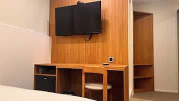 A bedroom with a wooden desk, a television mounted on the wall, a bed, and a wardrobe.