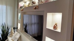 Een moderne woonkamer met een flatscreen televisie aan de wand, omringd door planken met decoratieve objecten en een potplant.