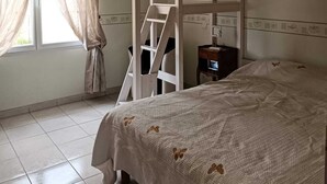 Een slaapkamer met een stapelbed, een trapje, een bureau en een raam met gordijnen.