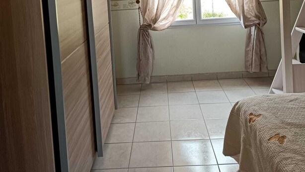 Een slaapkamer met een bed, een raam met gordijnen, een plafondventilator en een kledingkast.