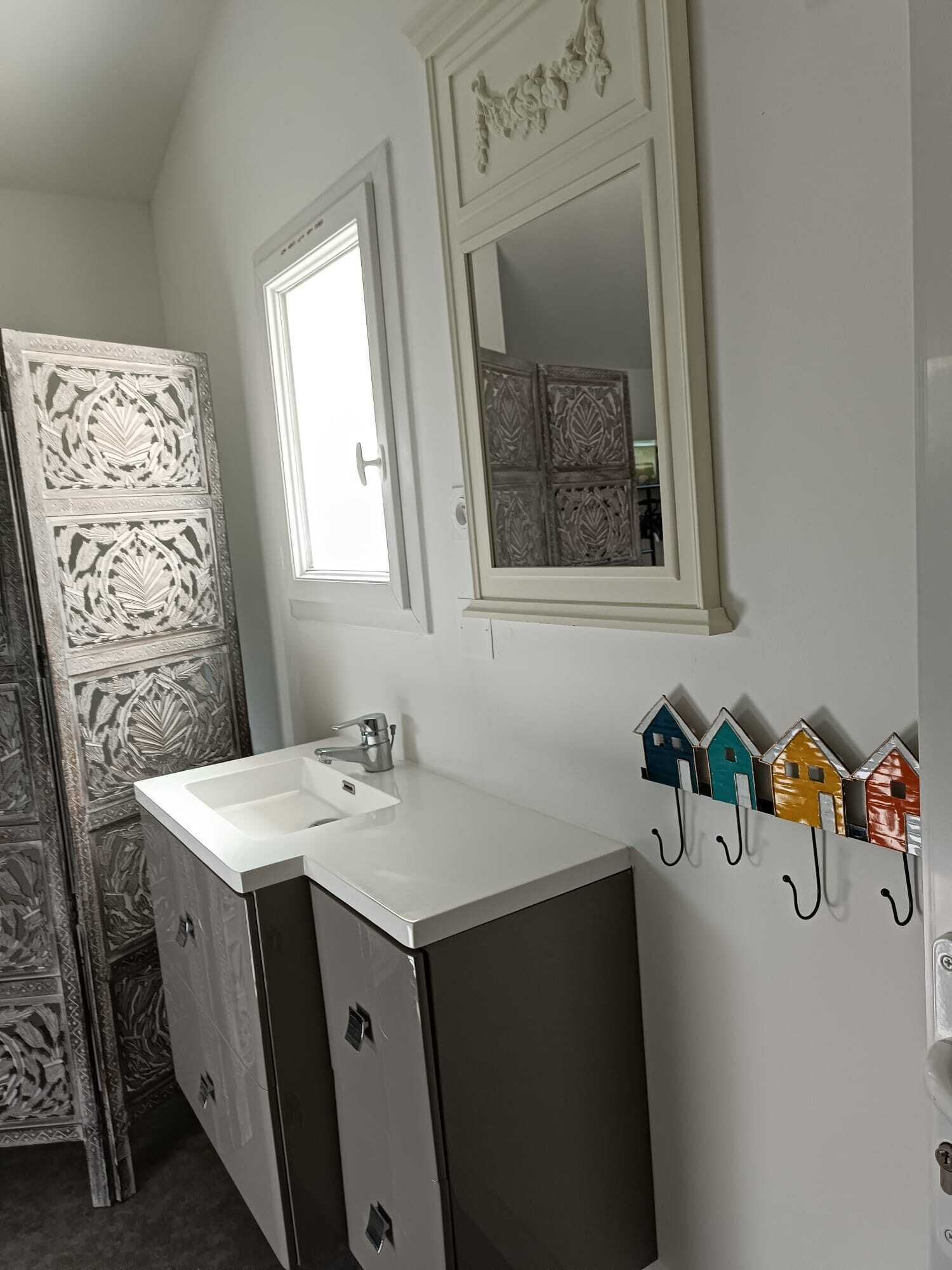 A bathroom with a white sink, two mirrors, and a decorative wall panel.