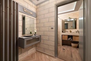 A modern bathroom with a 'Welcome' sign, a large mirror, and a vanity with a sink. - Kostas Nest (Ialisos)