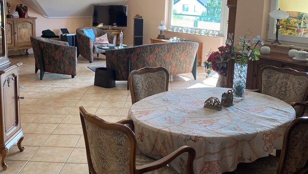 A dining area with a round table, chairs, and a television in the background.