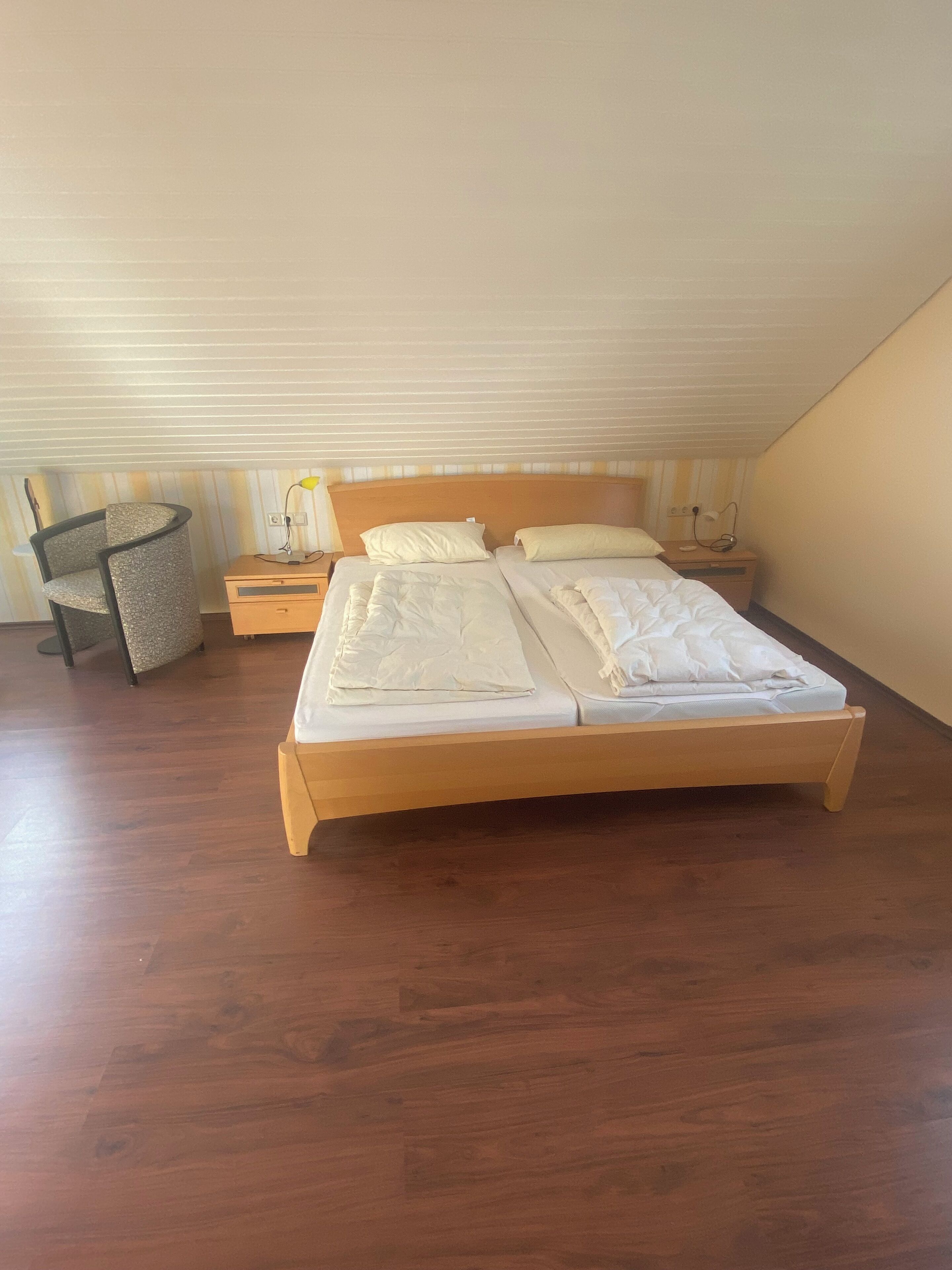 Un dormitorio con una cama de madera, dos mesitas de noche, una silla y una lámpara.