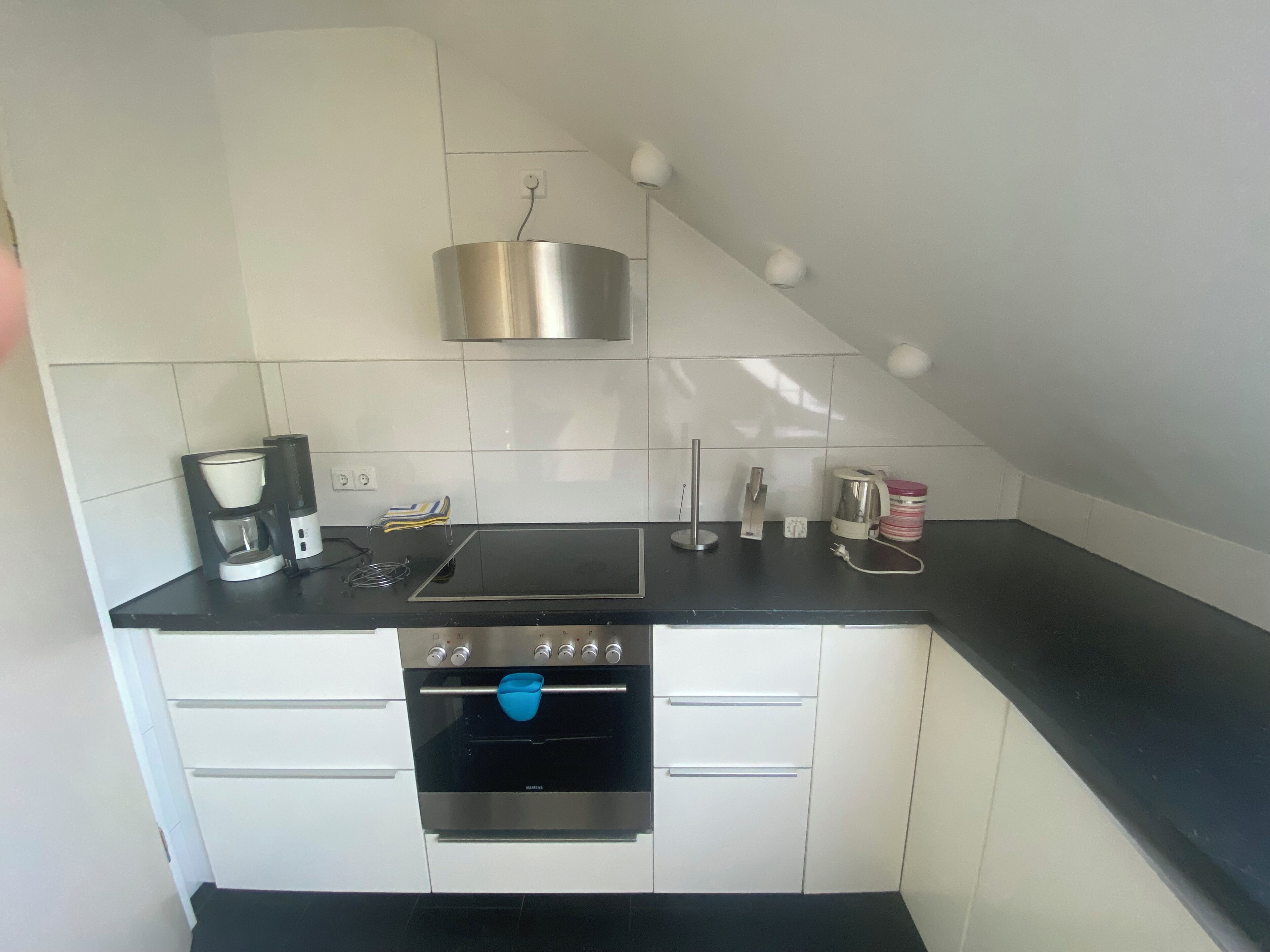 A compact kitchen with a built-in oven, a coffee maker, and a kettle on the countertop.